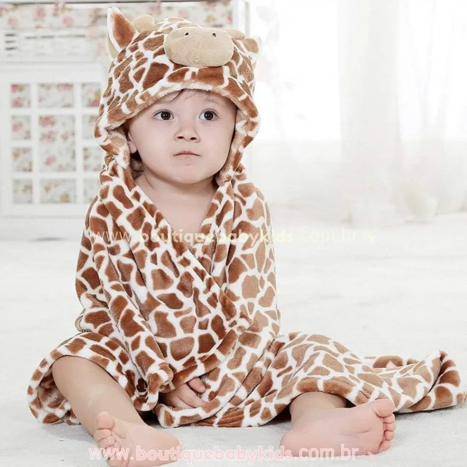 Bebê sentado com a toalha de girafa envolta no corpo, destacando o capuz com detalhes tridimensionais, incluindo orelhinhas e focinho acolchoado.