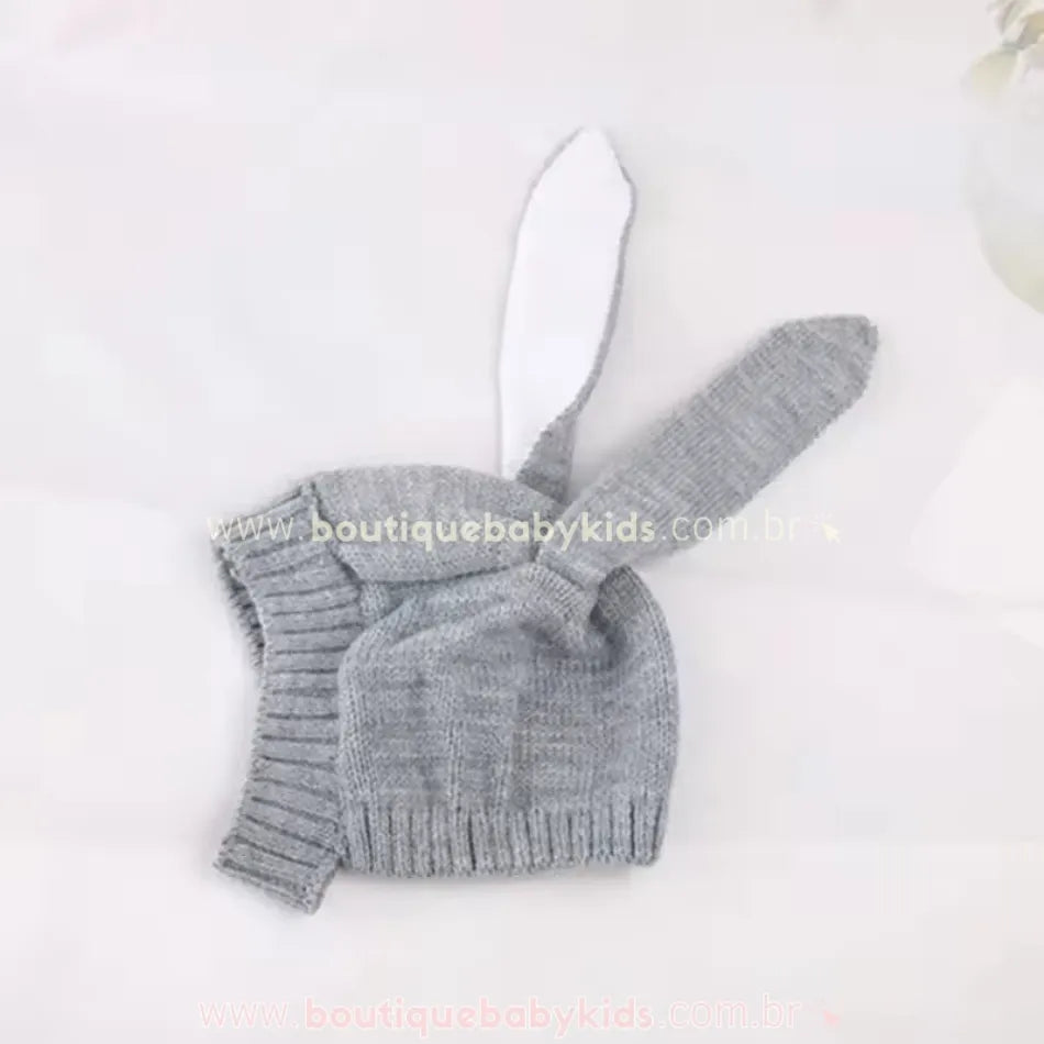 Touca de tricot cinza dobrada, com uma das orelhas flexionada, exibindo a textura do tecido e o acabamento.