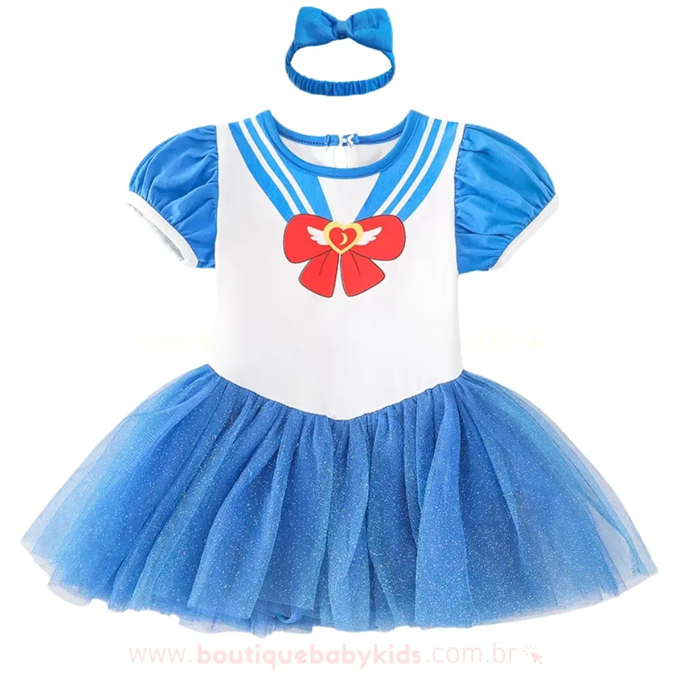 Vestido de bebê inspirado na Sailor Moon, com corpete branco e azul, estampa de laço vermelho com coração e asas, mangas bufantes e saia de tule azul brilhante. Acompanha uma faixa de cabelo azul combinando.