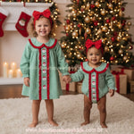 Irmãs vestindo Body e Vestido de Natal Clássico Xadrez Verde Bordado Papai Noel com Faixa de pé em tapete claro de mãos dadas com cenário natalino - Boutique Baby Kids