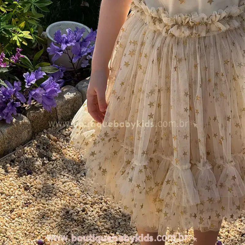 Detalhe da textura da saia do vestido infantil. Mostra a delicadeza do tule transparente sobreposto com estrelas douradas e o acabamento franzido na cintura.