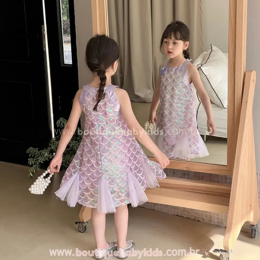 Criança em frente ao espelho mostrando a parte de trás do vestido de festa tema Sereia, com saia de tule e acabamento delicado.
