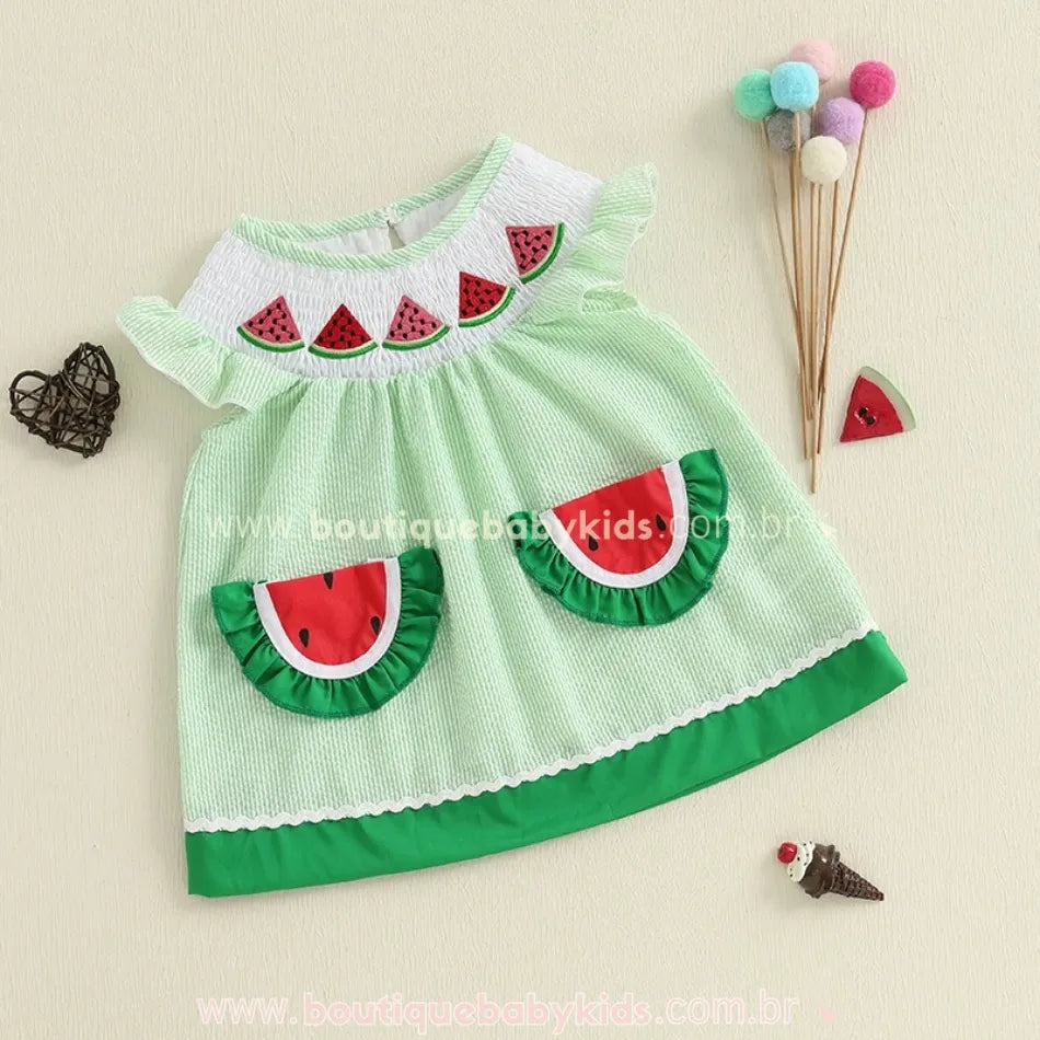 Vestido infantil temático de melancia com bolsos e babados, acompanhado de acessórios decorativos.