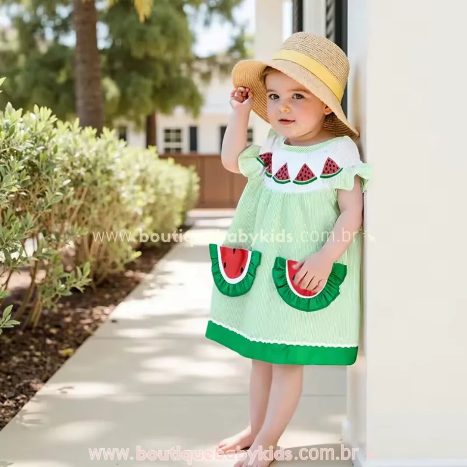 Menina usando o vestido melancia em ambiente externo ensolarado com chapéu de palha.