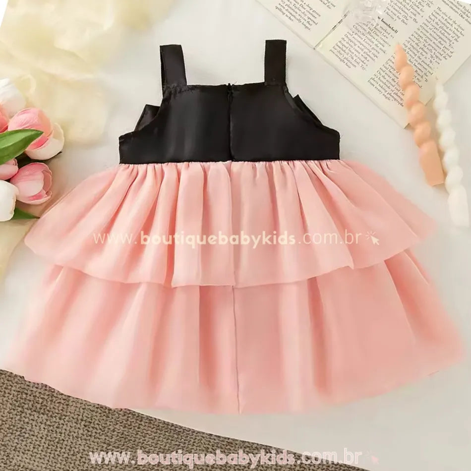 Vestido infantil rosa com busto preto e saia em camadas de tule, visto pela parte de trás.