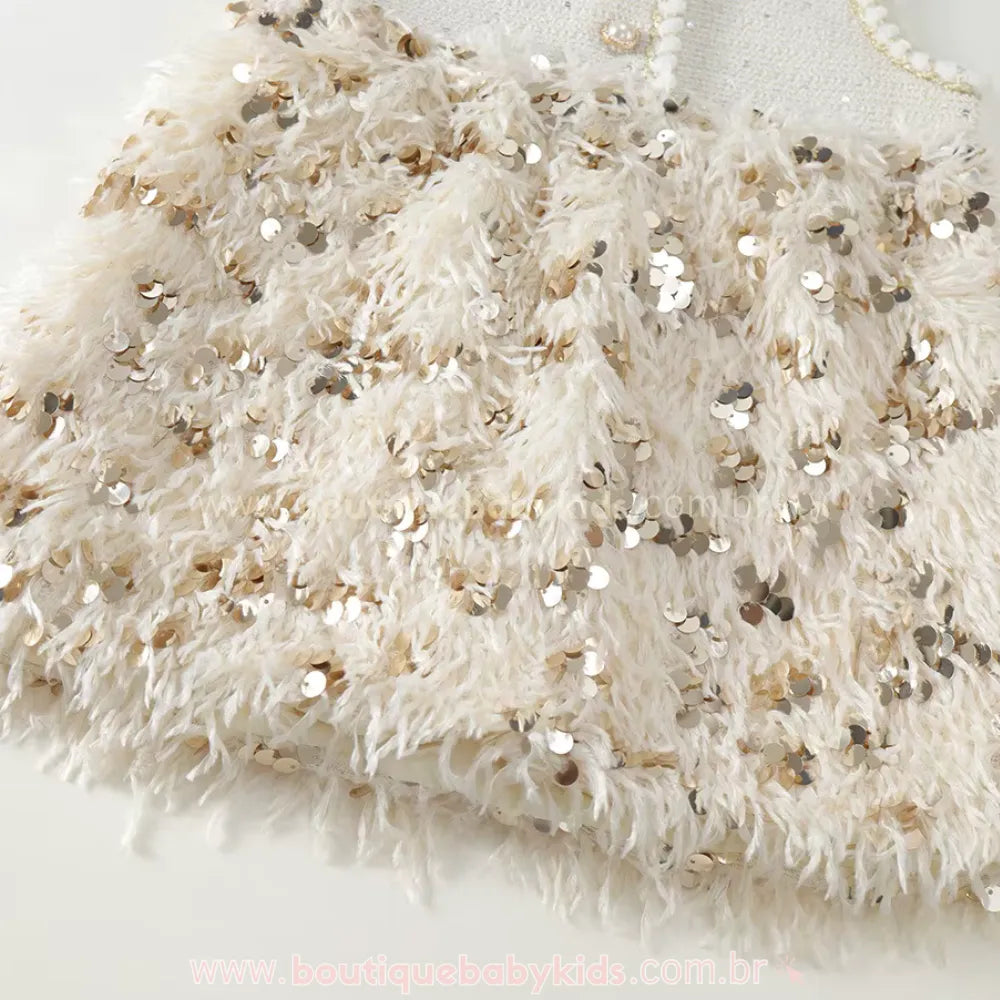 Close-up da textura da saia do vestido, mostrando a riqueza das plumas macias intercaladas com paetês dourados que proporcionam brilho suave.