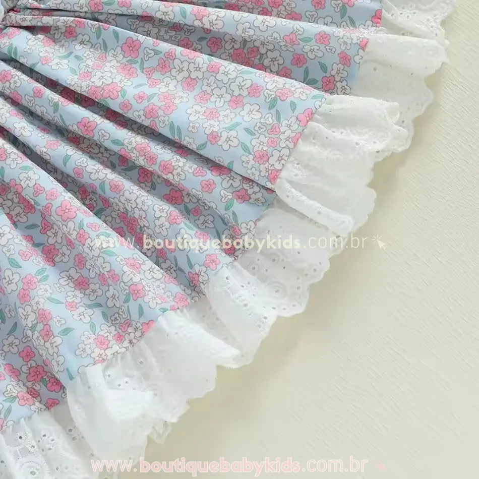 Saia do vestido em tecido azul floral, com babados de renda branca na barra, trazendo um toque clássico e delicado ao modelo.