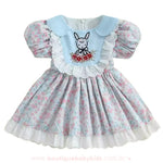 Vestido infantil azul floral com detalhes bordados de coelhinho e flores na parte frontal, gola arredondada azul clara e babados de renda branca ao redor do busto.
